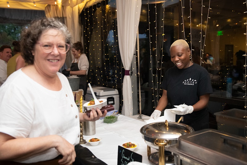 two smiling women, one being served by the other at the buffet