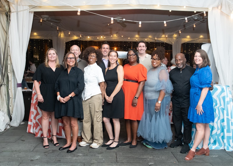 group of men and women smiling outside with string lights